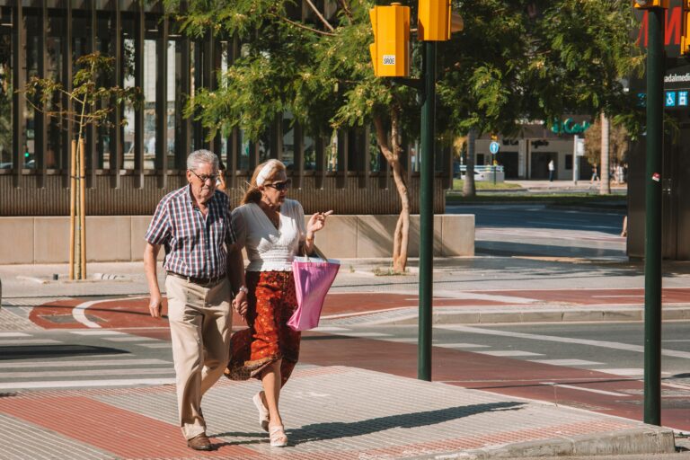 Senior couple crossing a sunlit street in Málaga, Spain, during a sunny day.