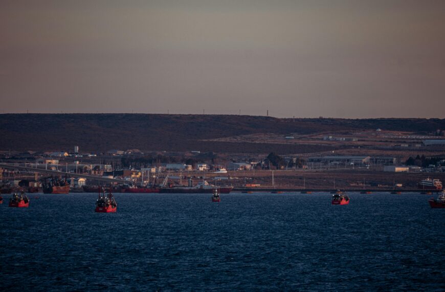 Distant view of fishing boats in a harbor at sunset with an industrial backdrop.