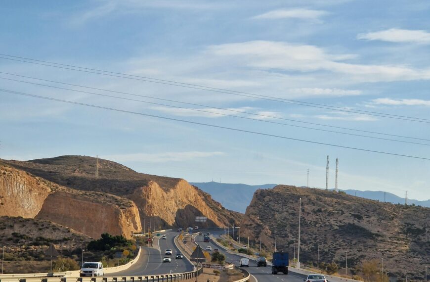 A highway stretches through the desert hills of Almería, Spain under a clear blue sky.
