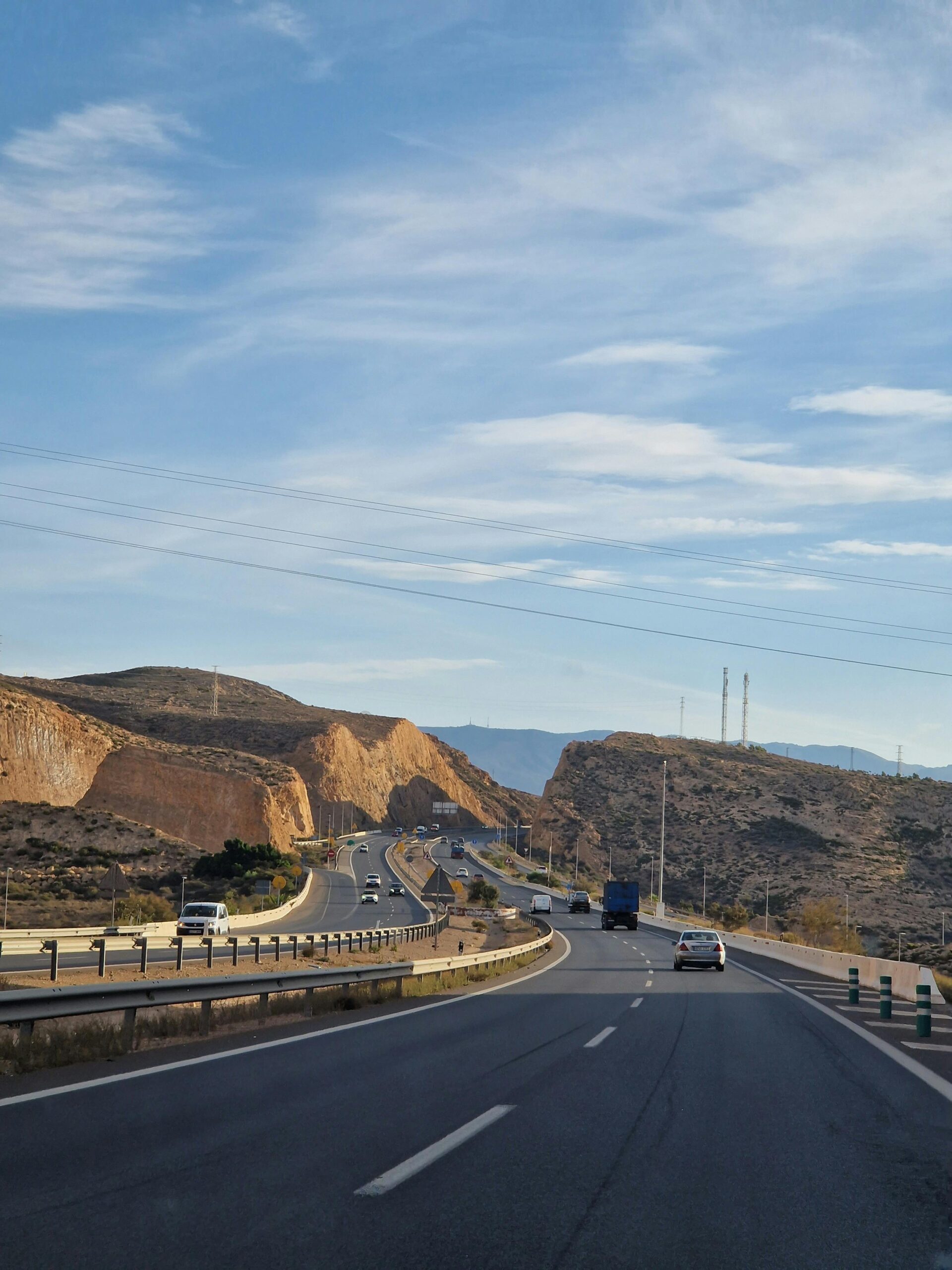 A highway stretches through the desert hills of Almería, Spain under a clear blue sky.